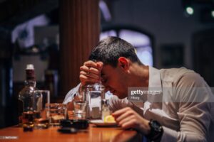 Sad drunk man sitting at bar counter, drinking whiskey and tequila.